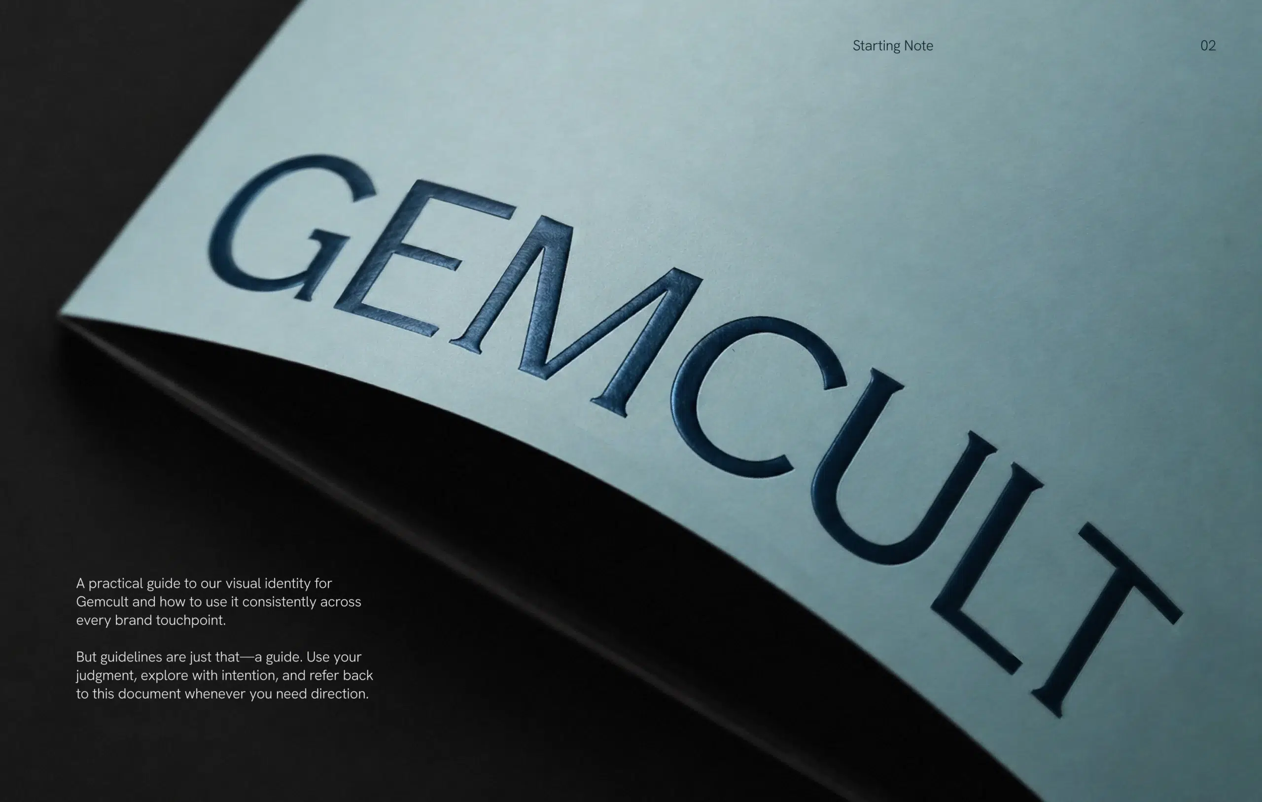 A close-up of a light blue booklet with the title “GEMCULT” embossed on the cover, placed on a dark surface. Text about brand identity guidelines appears on the left side, highlighting elements of luxury packaging design and thoughtful brand strategy.